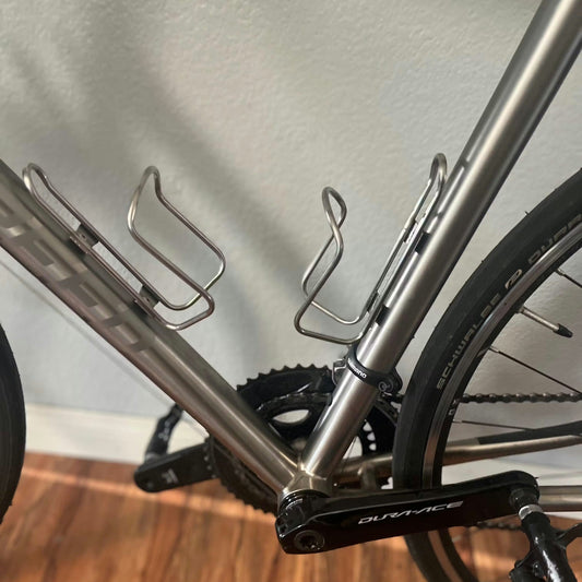 Close-up of a bicycle frame with water bottle holders on a wooden floor.