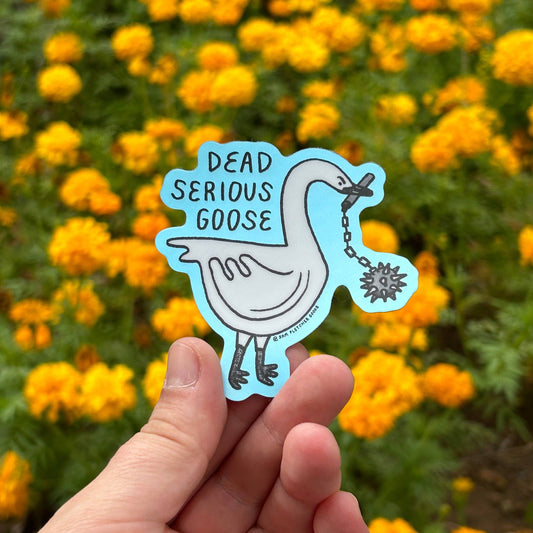 A hand holds a die-cut sticker featuring a cartoon goose with the text 'DEAD SERIOUS GOOSE' against a blurred background of yellow flowers.