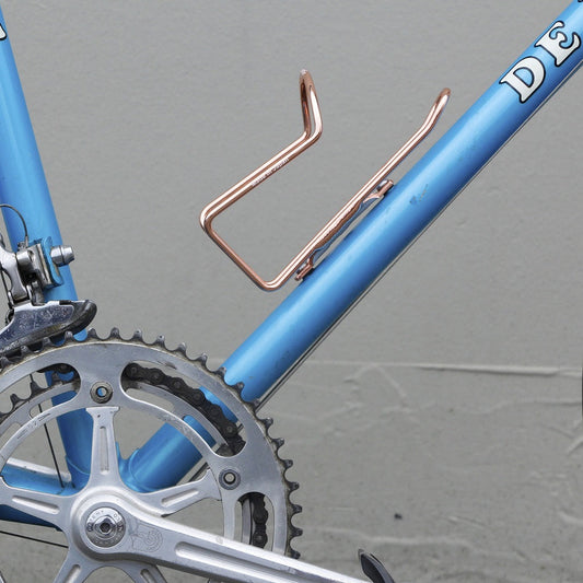 Close-up of a blue bicycle with a copper water bottle holder on a gray background