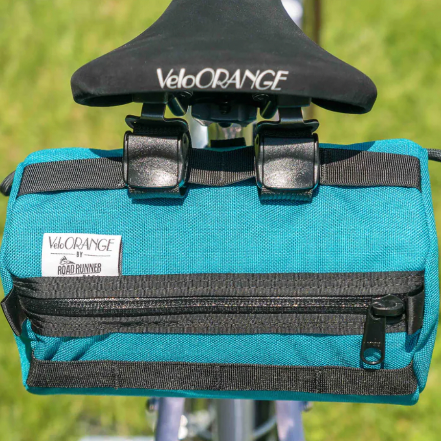 Blue bicycle saddle bag with black straps and VeloOrange branding on a blurred green background