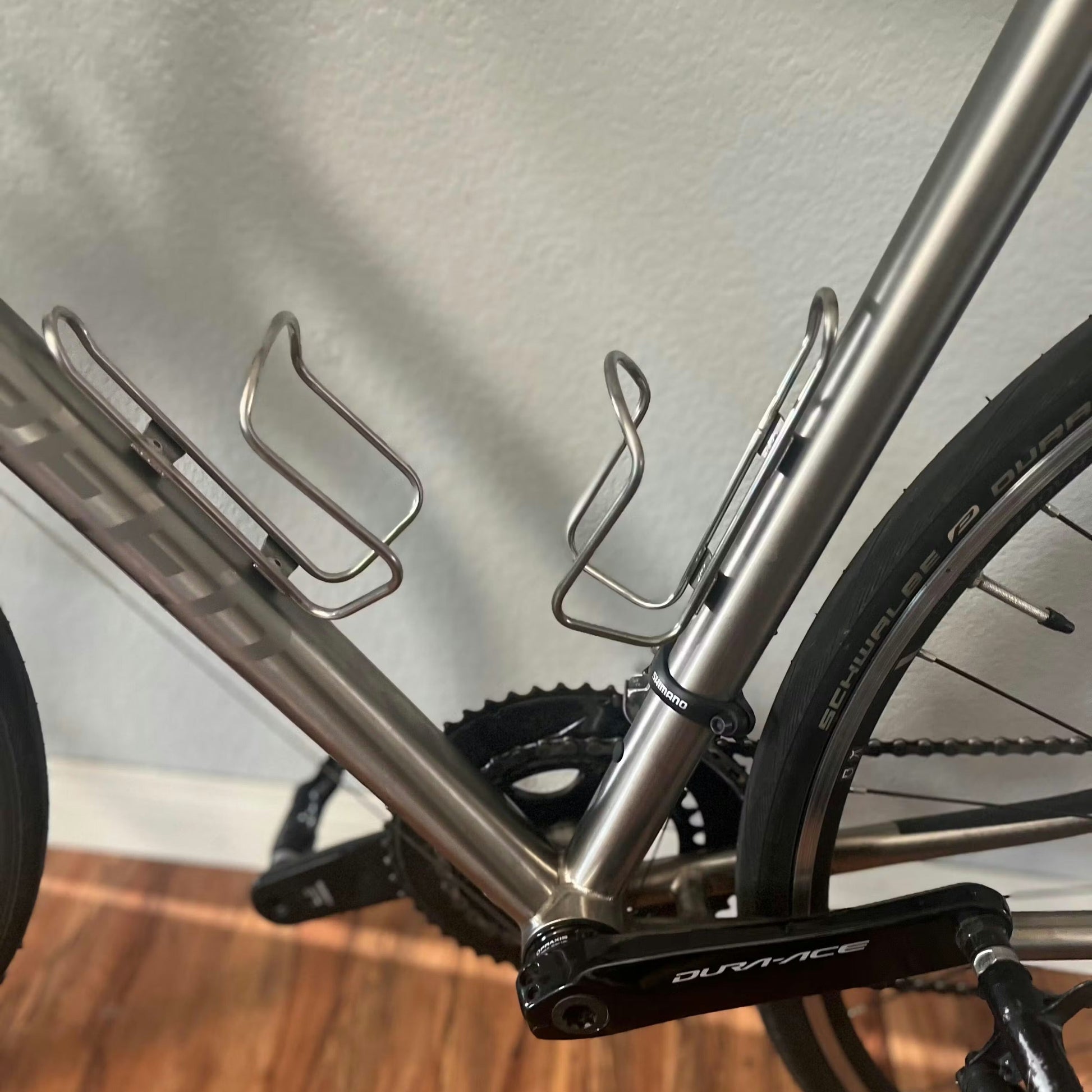 Close-up of a bicycle frame with water bottle holders on a wooden floor.