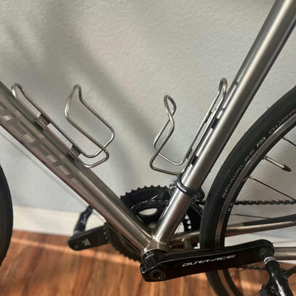 Close-up of a bicycle frame with water bottle holders on a wooden floor.