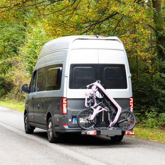 Folded FOLD eFold electric cargo bike standing on both wheels on a hitch-mounted platform bike rack behind a van