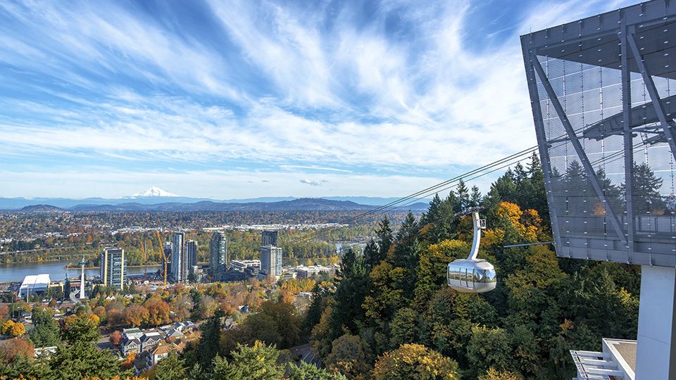 OHSU EBike Voucher Header Image. Gondola lift system with a cityscape and trees in the background