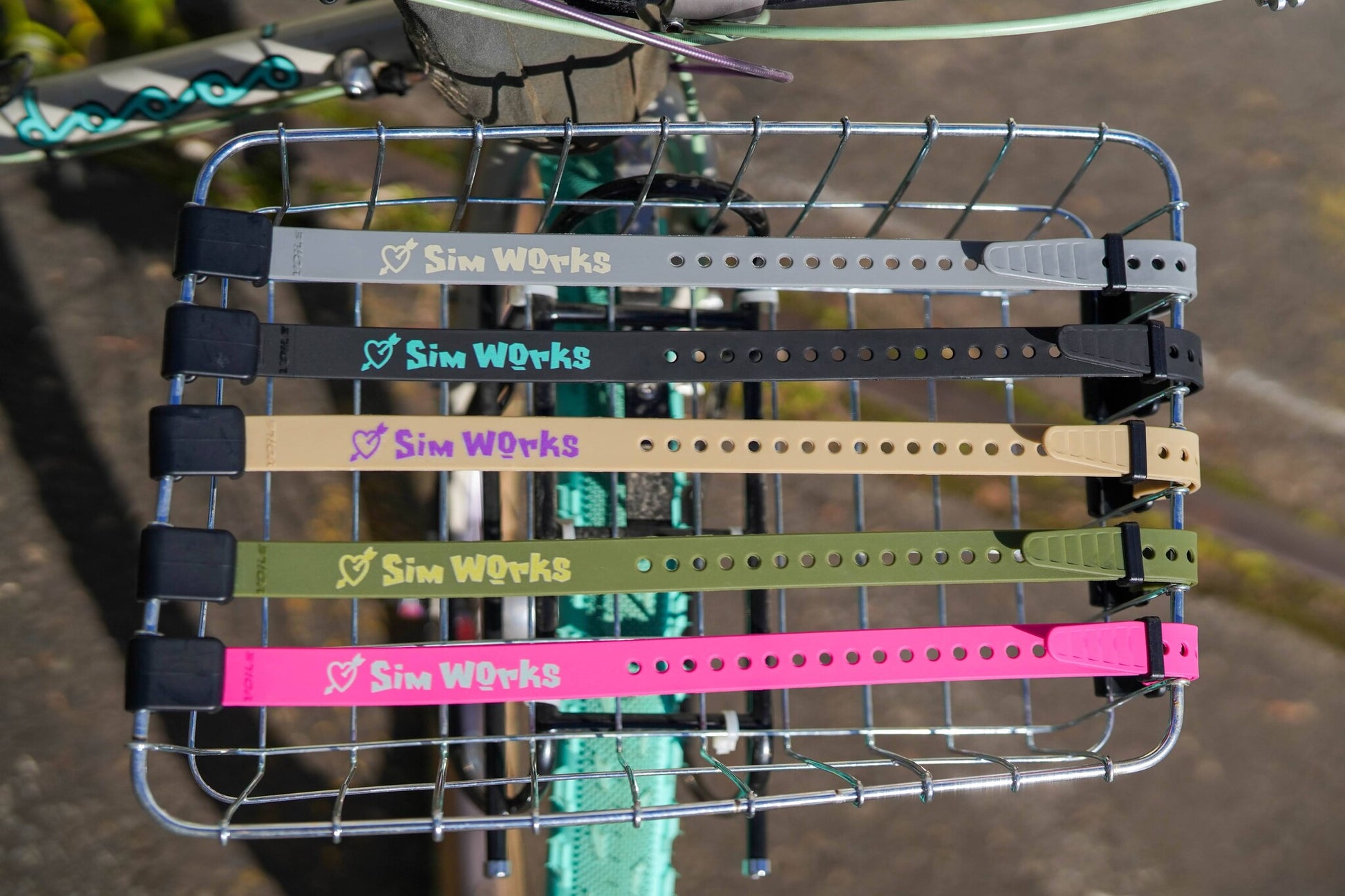 Bicycle basket with multiple straps labeled 'Sim Works' on a blurred background