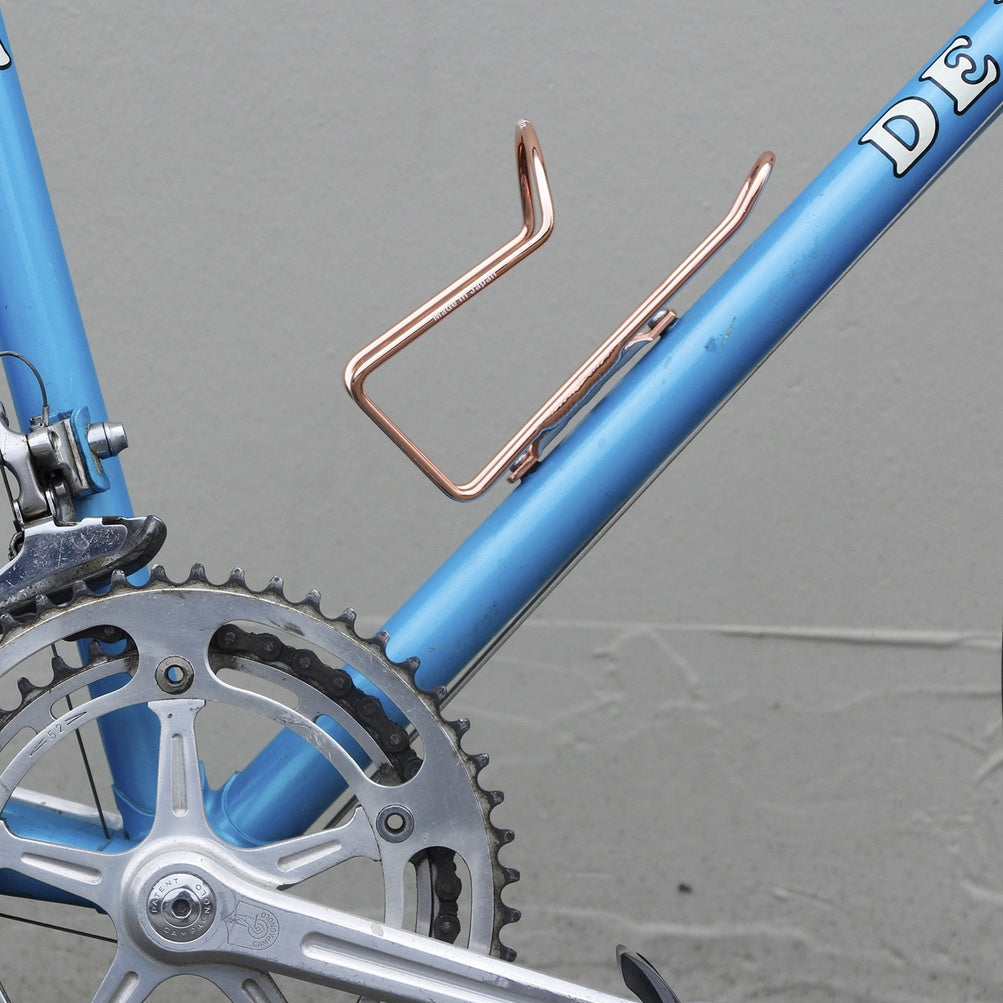 Close-up of a blue bicycle with a copper water bottle holder on a gray background