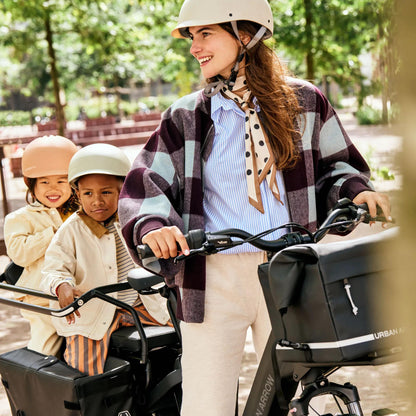 Woman riding a cargo bike with two children in a park