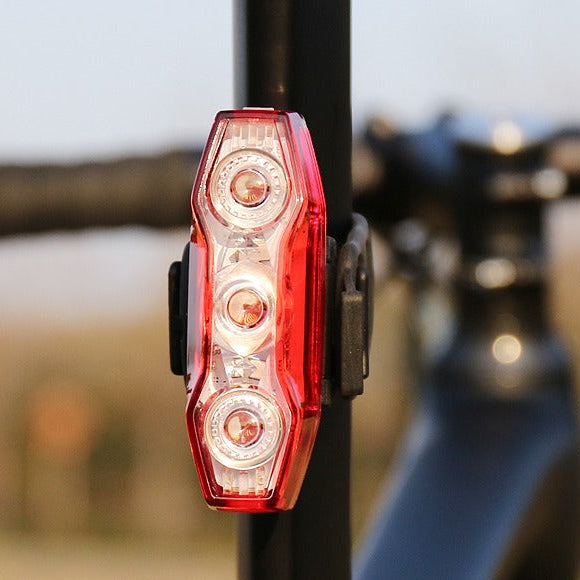 Red bicycle tail light attached to a bike frame with a blurred outdoor background