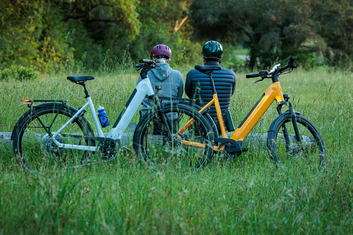 Two riders resting in a meadow beside their Gazelle e-bikes