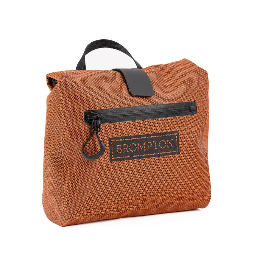 An orange-brown Brompton waterproof bag with black trim, a top handle, and a front zippered pocket on a white background.