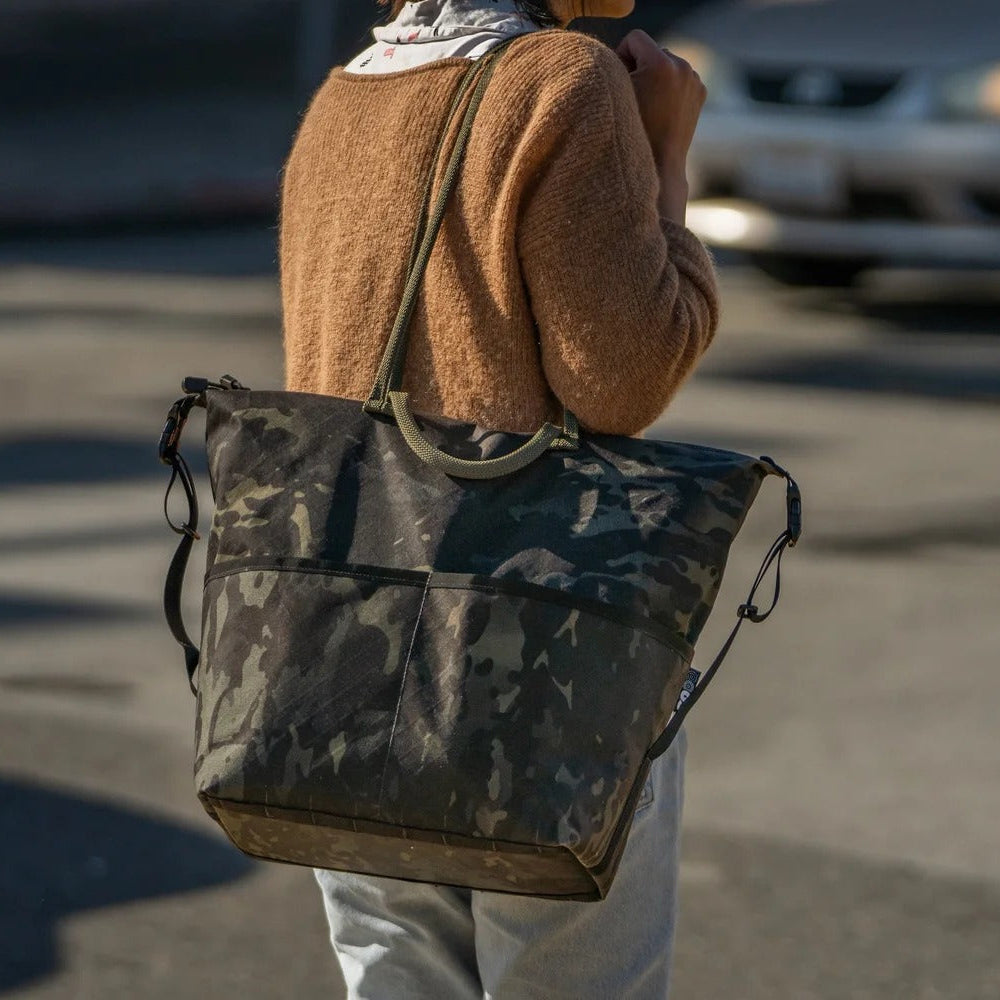 Person holding a camouflage backpack in an urban setting