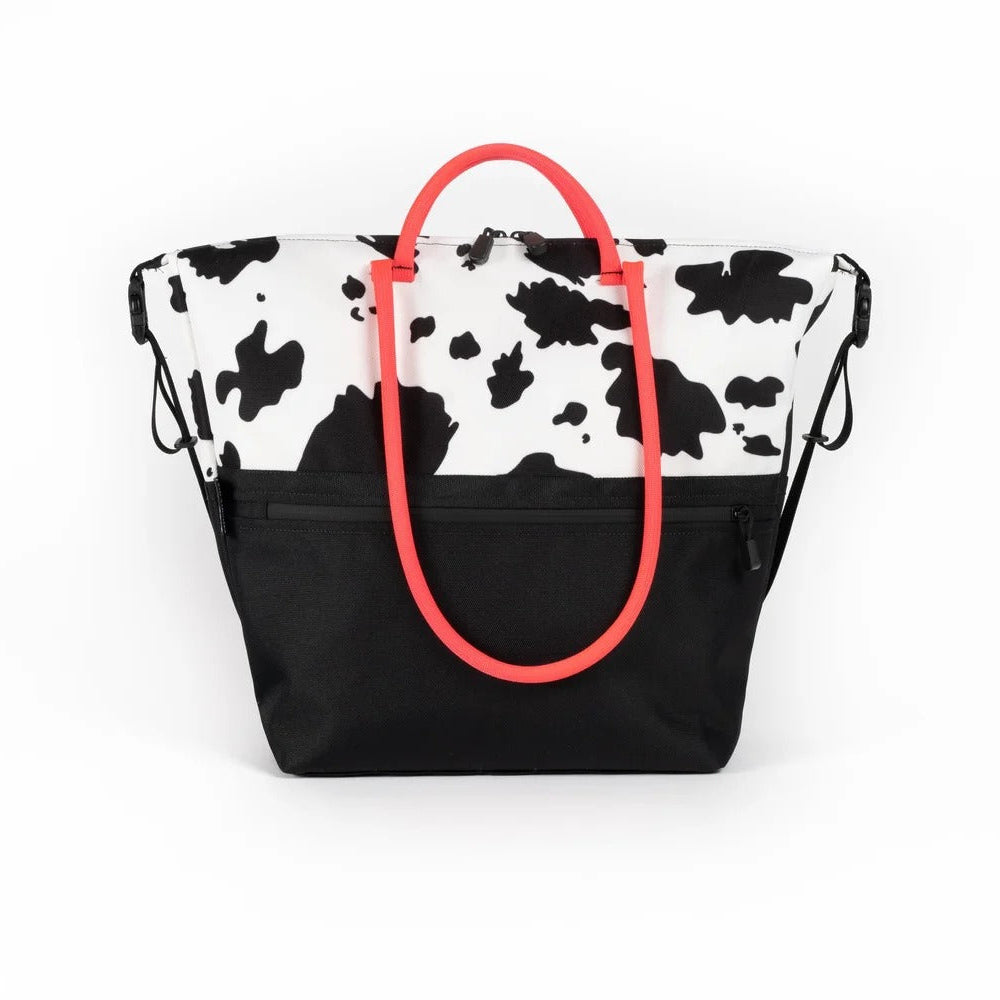 Tote bag with cow print top half and black bottom half, featuring a bright red handle on a white background.