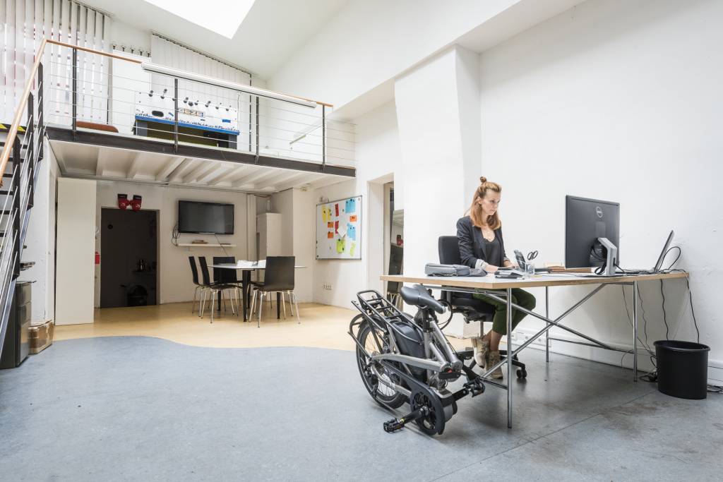 Person working at a desk with a Tern folding bicycle on wheels in an office setting