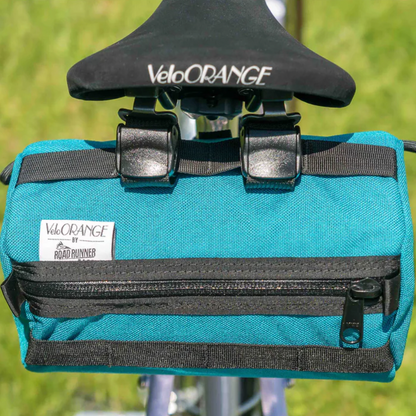 Blue bicycle saddle bag with black straps and VeloOrange branding on a blurred green background